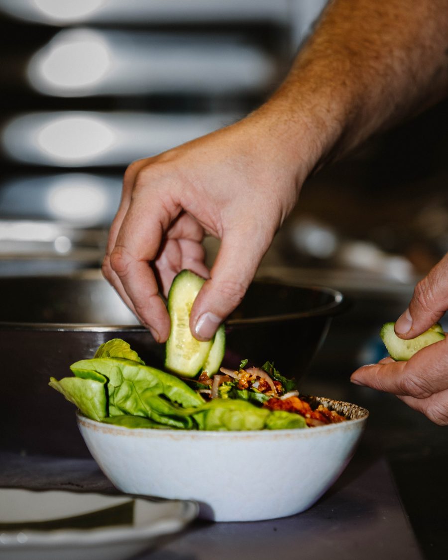 A chef placing sliced cucumber onto a bowl of lettuce and spiced filling