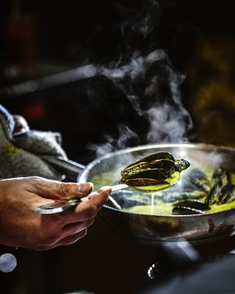 Steaming mussels lifted from a pan of green broth